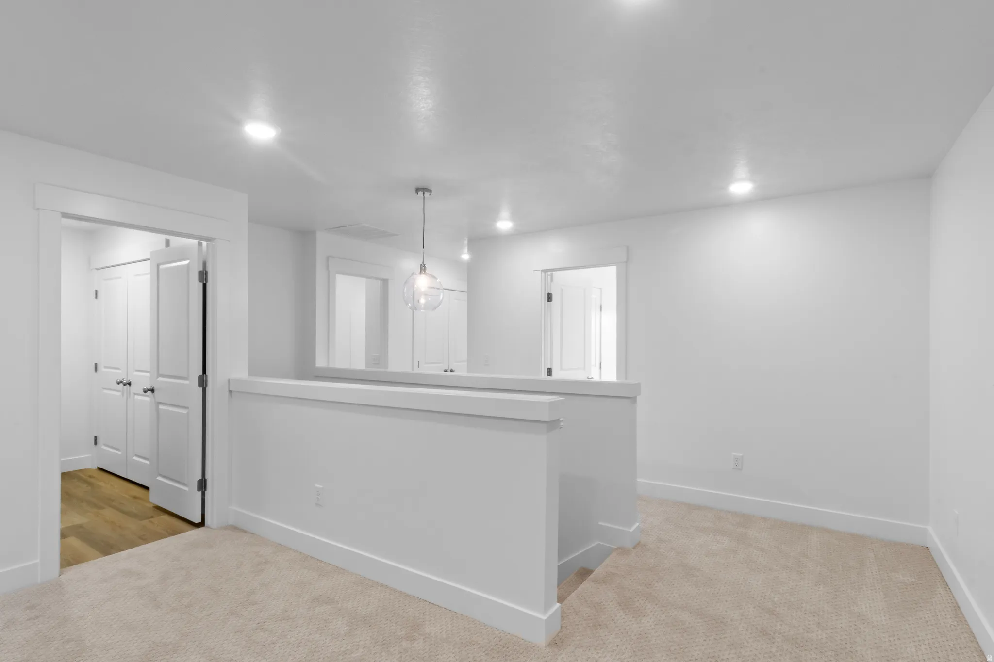 Bright open room featuring light-toned carpet flooring, recessed lighting, and a modern glass pendant light fixture