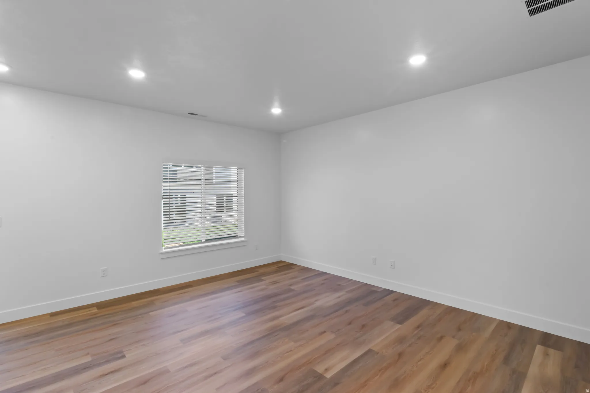 Spacious room featuring wood-finish flooring, white walls, and recessed lighting