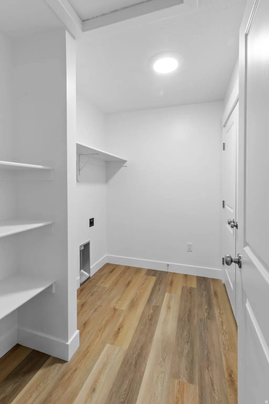 Laundry area featuring wood-finish flooring, built-in shelving, a wall outlet, and dryer vent hookups