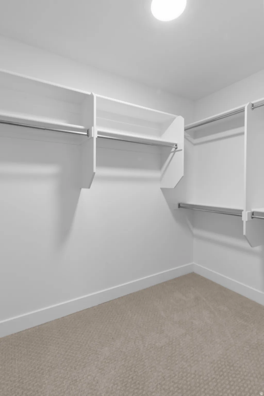 Walk-in closet with built-in shelving, chrome hanging rods, recessed ceiling light, white walls, and neutral-toned carpeting