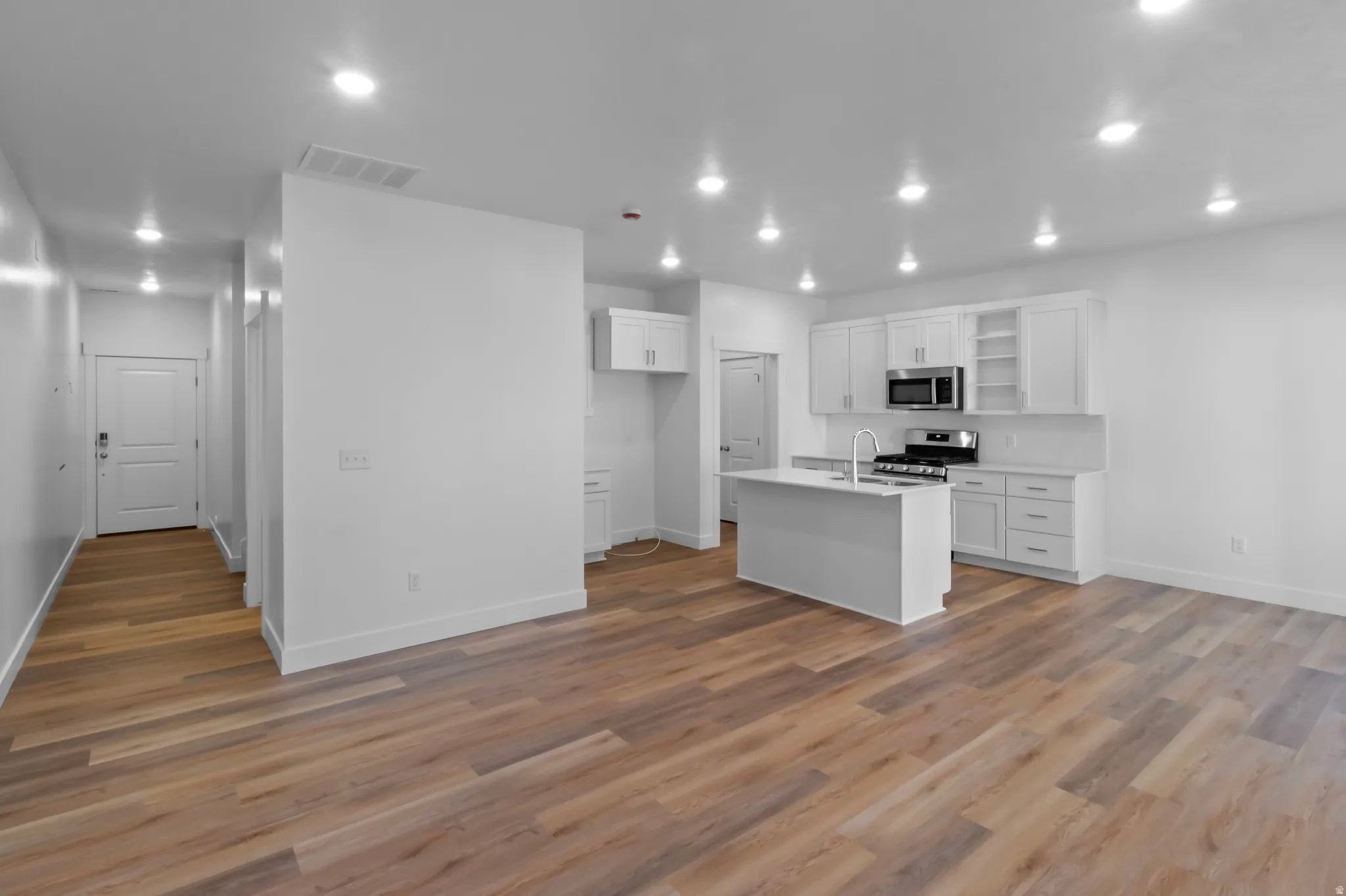 Open-concept living space featuring wood-finish flooring, recessed lighting, and a kitchen with white cabinetry