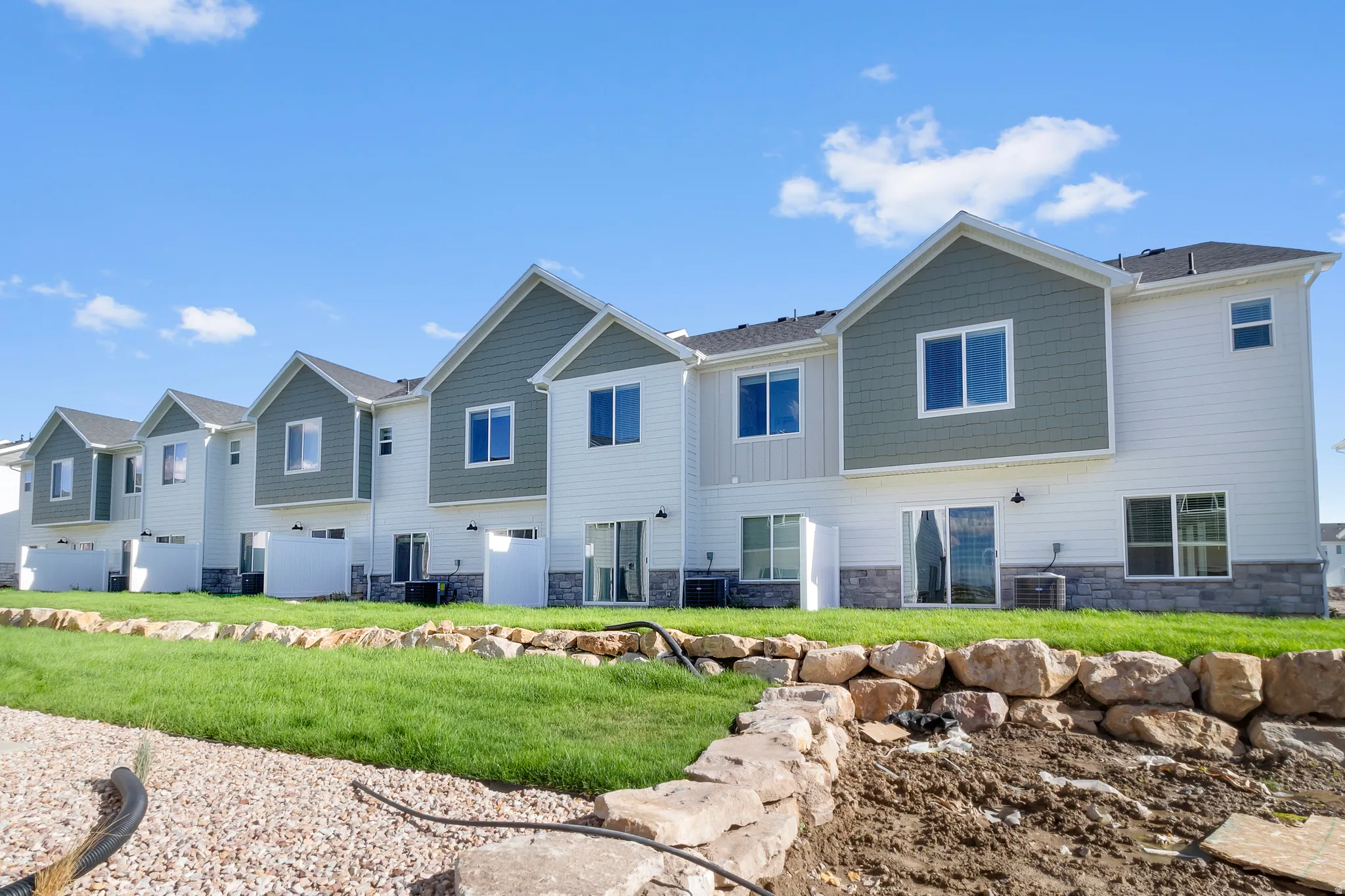 Row of contemporary townhomes featuring white siding, green-gray shingle accents, and stone veneer foundations
