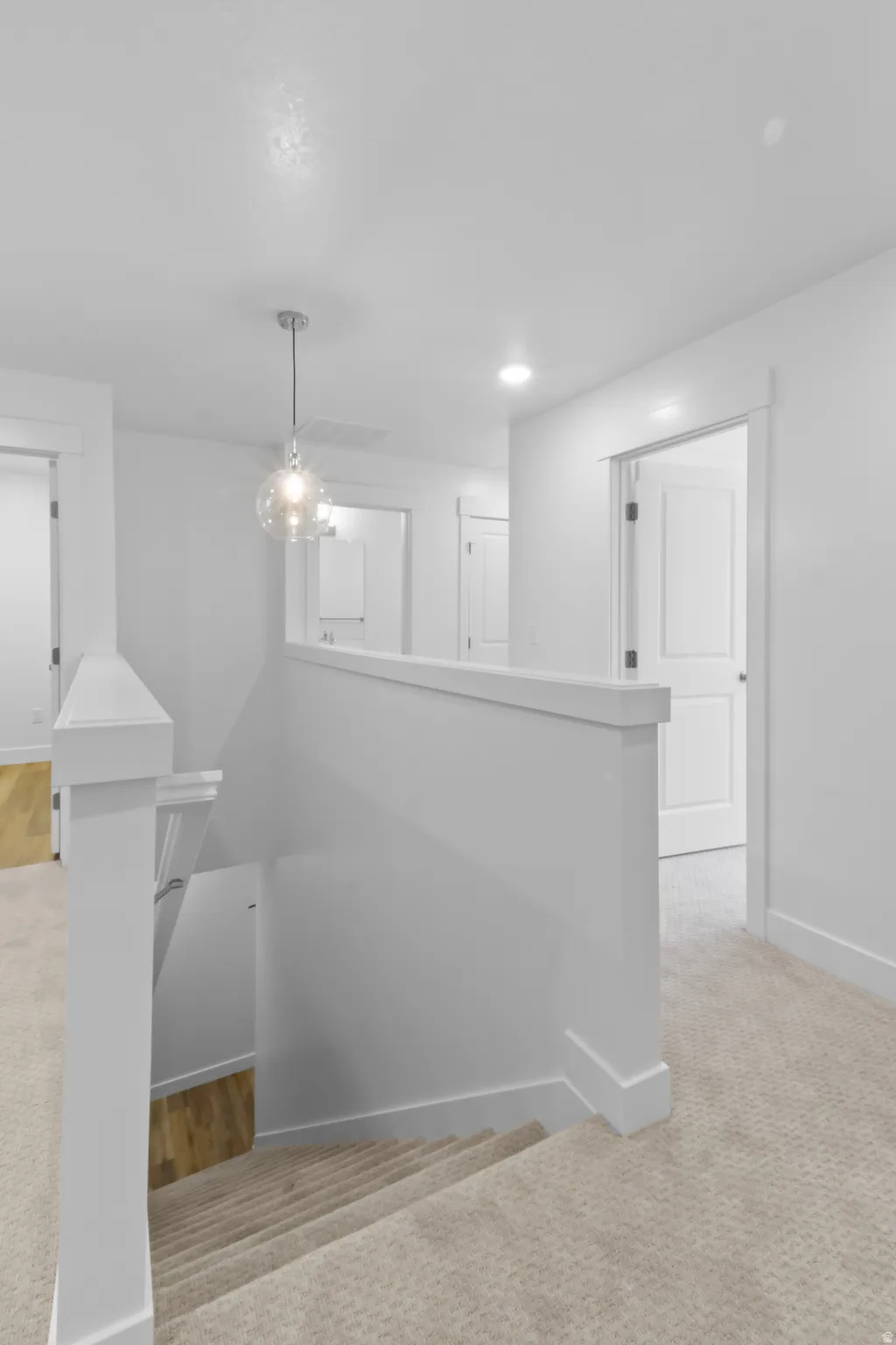 Carpeted staircase with white balustrade and contemporary pendant light fixture