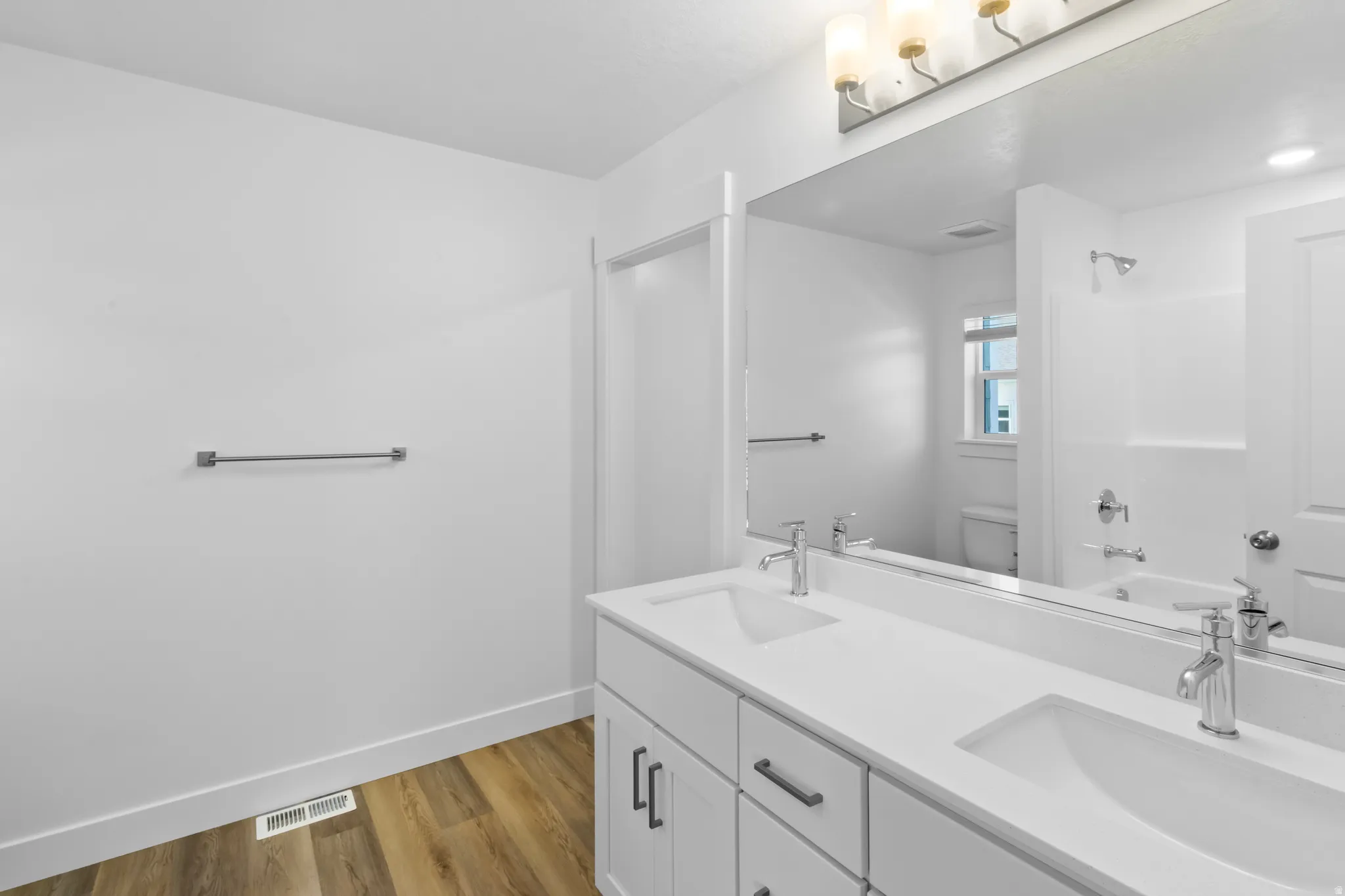 Bathroom featuring a double vanity with white countertops and integrated sinks, chrome fixtures, and wood-finish flooring