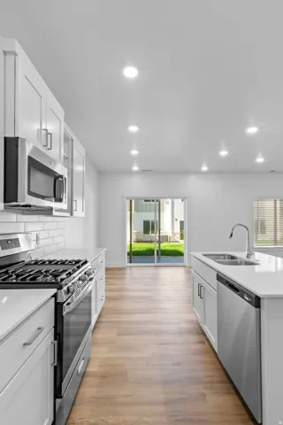 Modern kitchen featuring white cabinetry, stainless steel appliances, light-toned wood-finish flooring, and recessed lighting