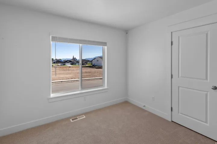 Bright interior room featuring a large window with white trim, neutral carpet flooring, and a paneled door