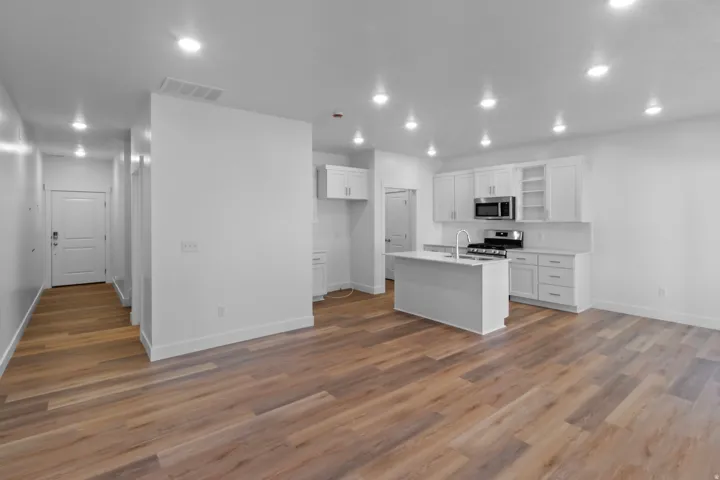 Open-concept living space featuring wood-finish flooring, recessed lighting, and a kitchen with white cabinetry