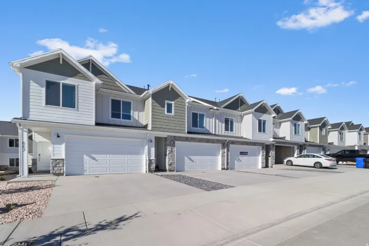 Contemporary townhome featuring a two-car garage, white siding, and stone accents