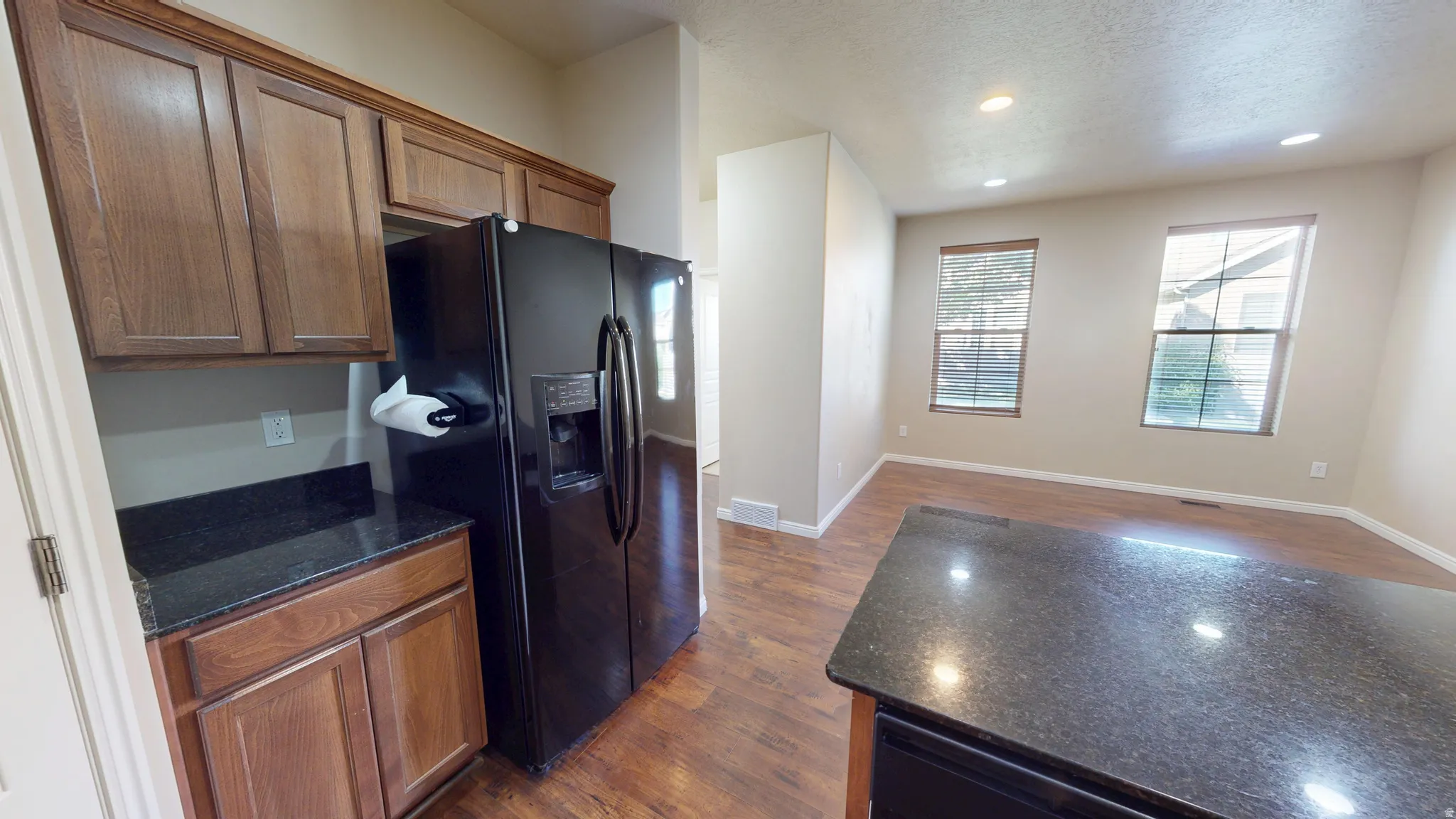Kitchen featuring wood cabinetry, dark granite-style countertops, and a black side-by-side refrigerator