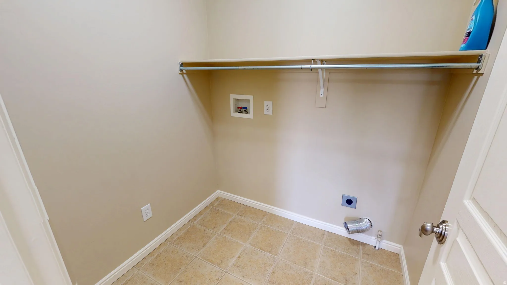 Utility area featuring beige wall paint, light-toned tile flooring, and a built-in shelf with a clothing rod