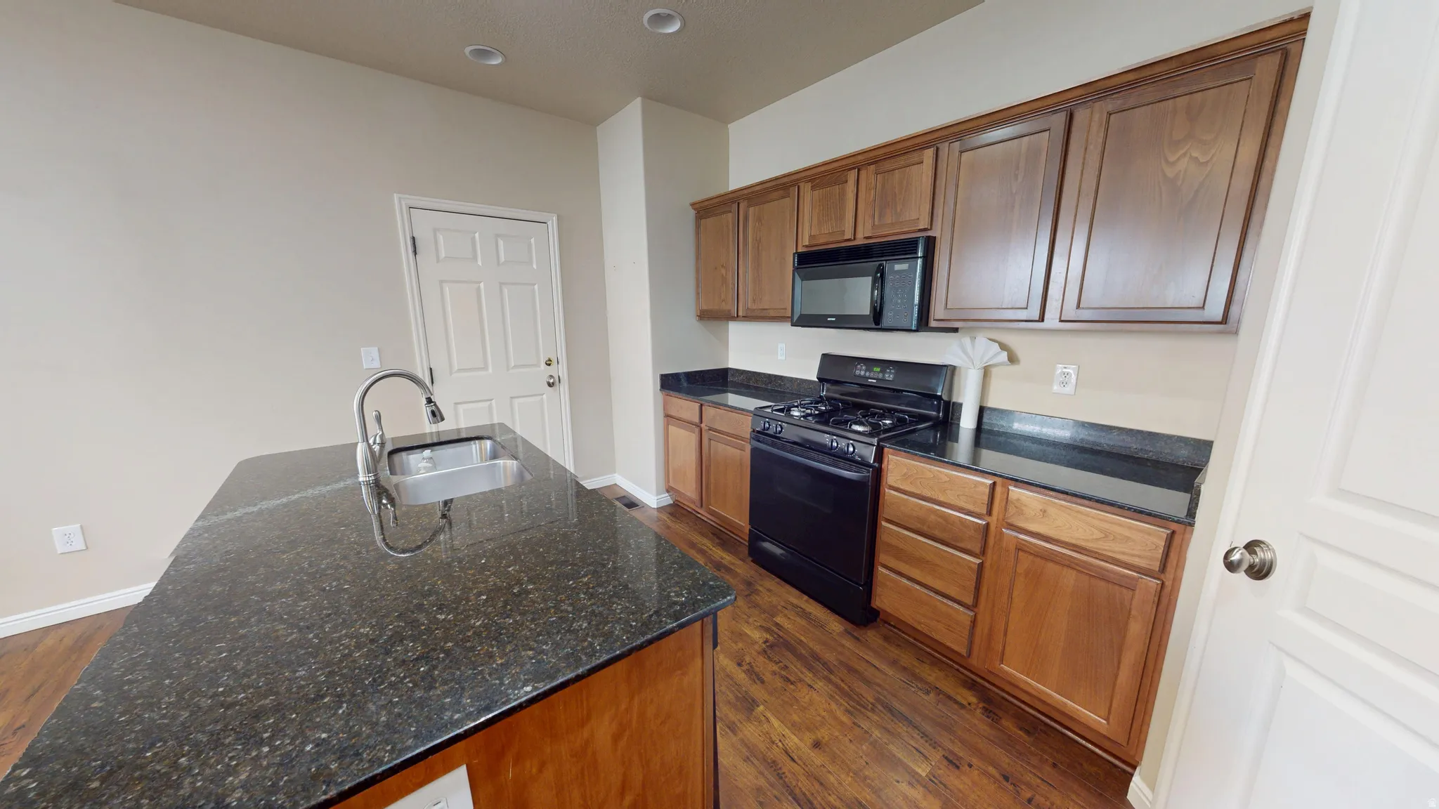 Kitchen featuring a dark speckled countertop island with an undermount sink and a brushed nickel faucet