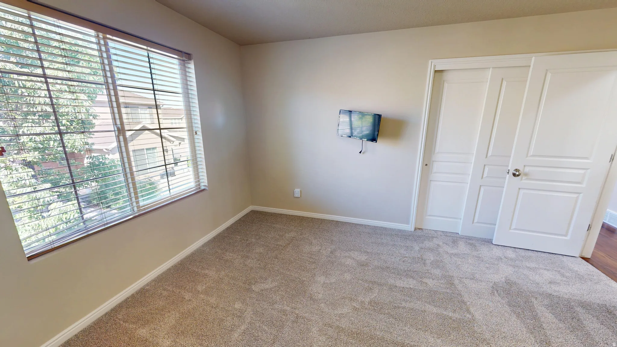 Neutral tone wall paint, textured carpet flooring, white trim, and a window with horizontal blinds