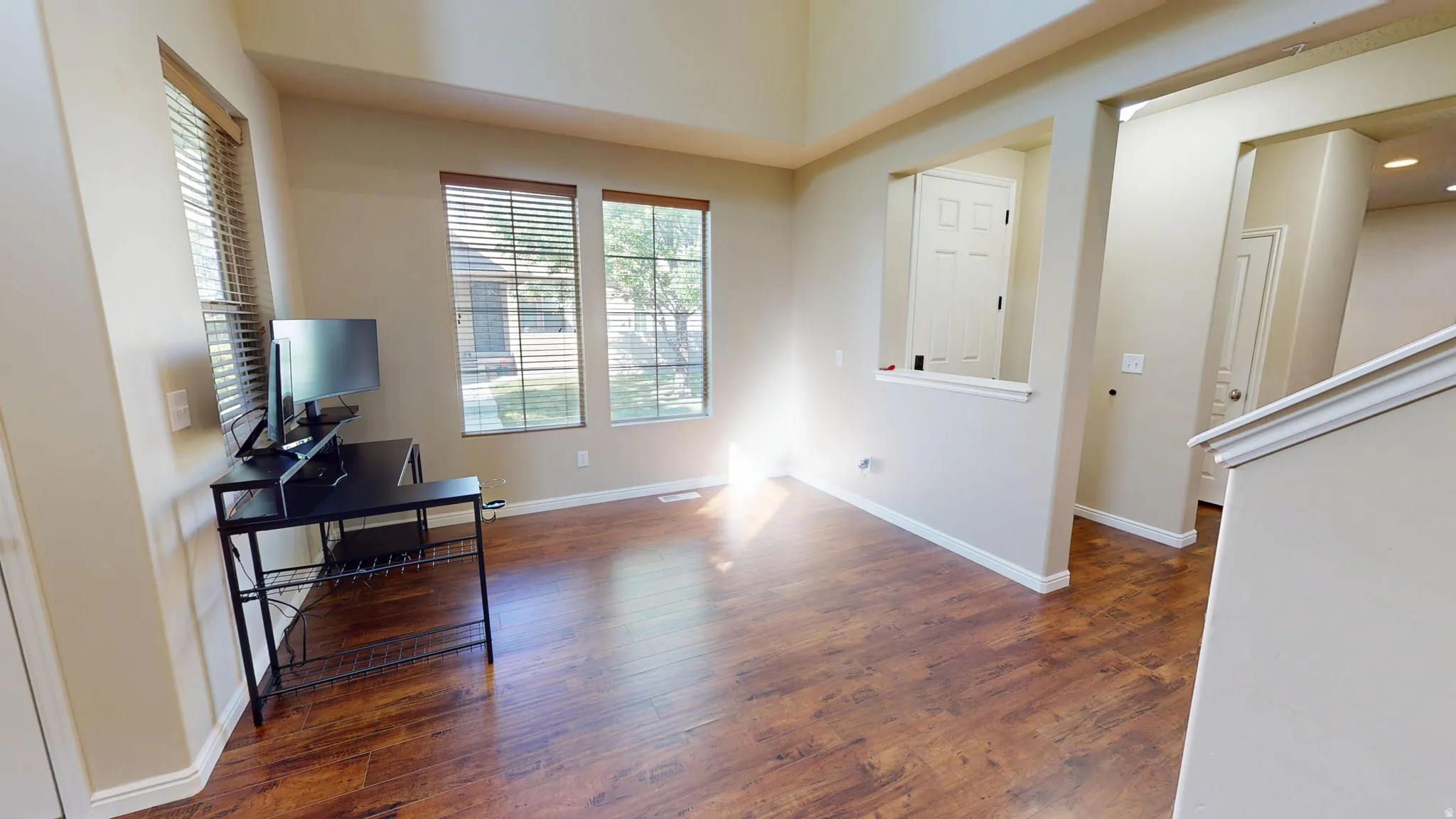 Spacious room with wood-finish flooring, multiple windows with blinds, and neutral wall paint