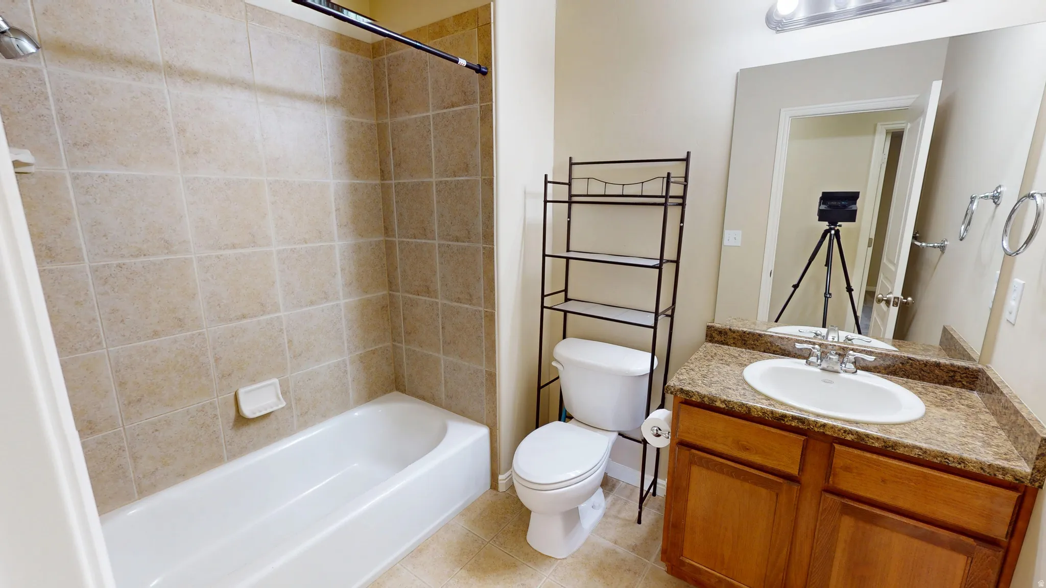 Full bathroom featuring a white porcelain tub with tiled surround, a toilet, and a vanity with a drop-in sink, dark speckled countertop, and wood-finish cabinetry