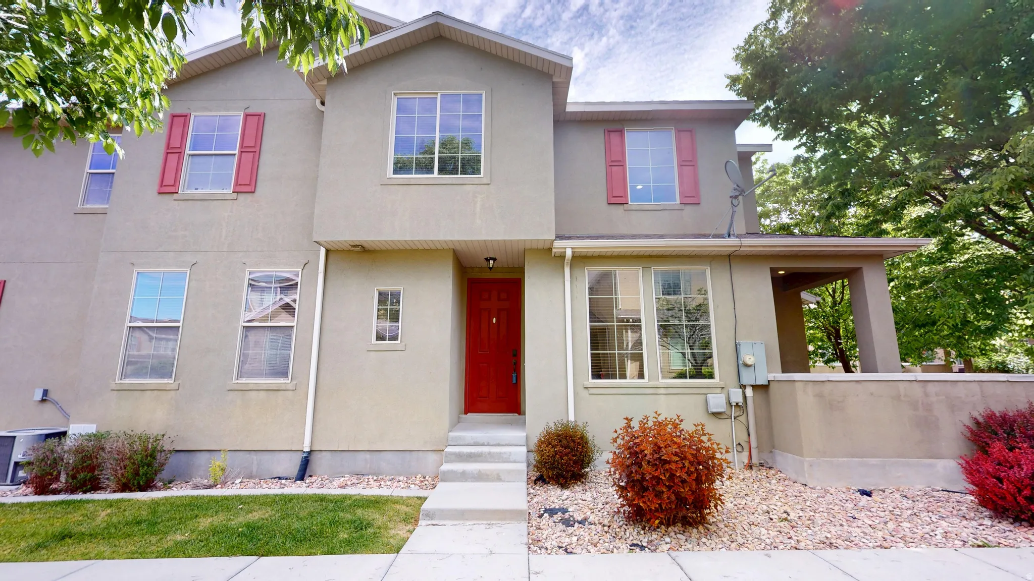 Multi-level stucco exterior featuring a prominent red entry door, red window shutters, and a covered patio area