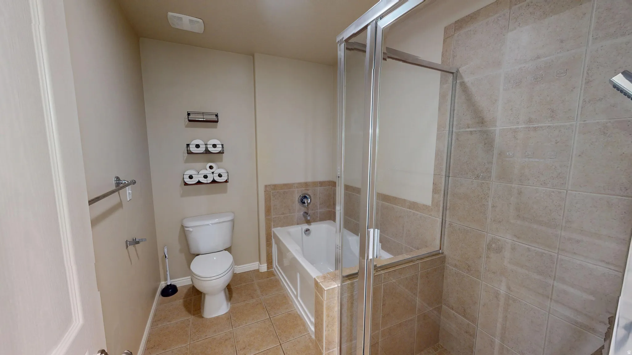 Bathroom featuring a tiled shower enclosure with glass panels, a white bathtub with tile surround, a white toilet, and neutral-toned floor tiling