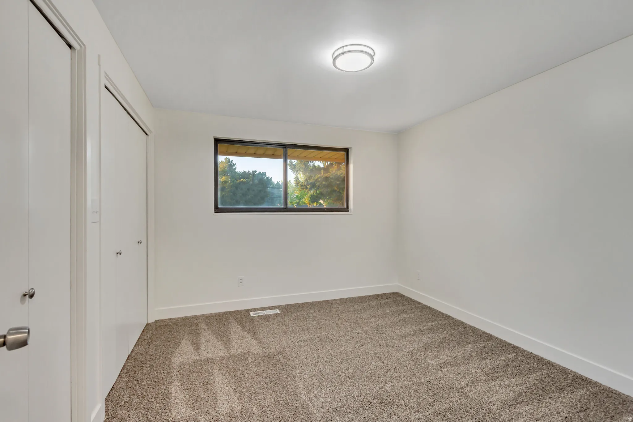 Carpeted room featuring a double closet with bi-fold doors, a single window, white baseboards, and a flush-mount ceiling light fixture