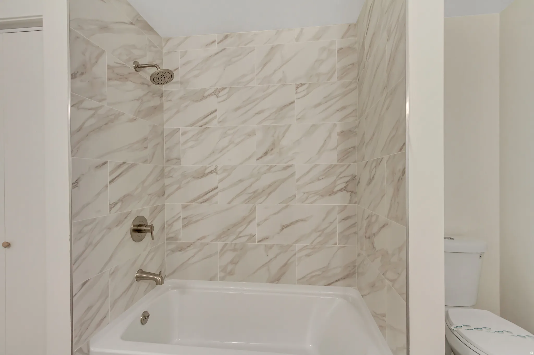 Bathtub with tiled shower surround featuring a rain-style shower head and a separate tub spout