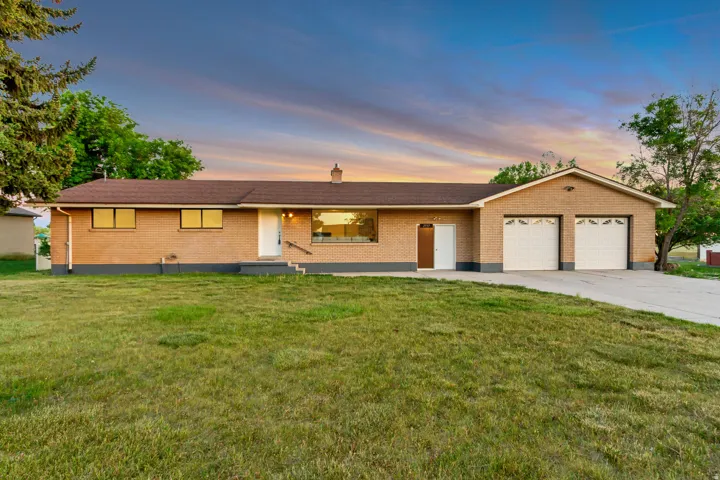 Brick exterior featuring a hip roof, integrated two-car garage with white paneled doors, and a concrete driveway
