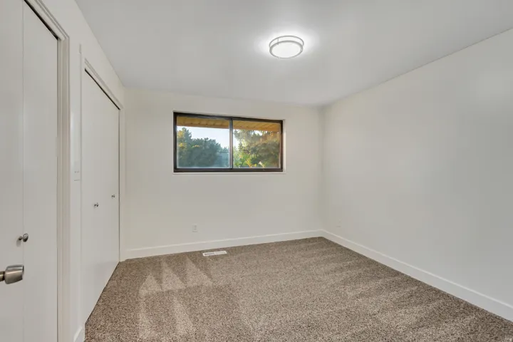 Carpeted room featuring a double closet with bi-fold doors, a single window, white baseboards, and a flush-mount ceiling light fixture
