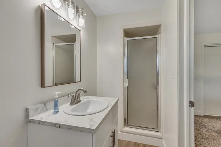 Bathroom featuring a single vanity with a white countertop and oval under-mount sink, brushed nickel faucet, and framed mirror with a three-light vanity fixture