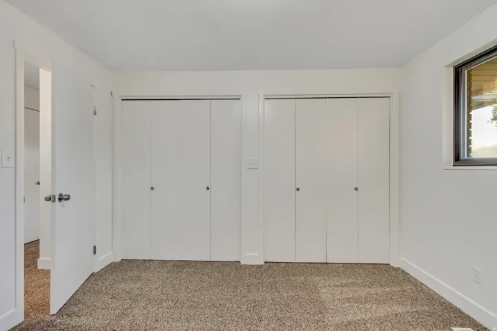 Interior room featuring neutral-toned carpeting, white walls, and two bi-fold closet doors