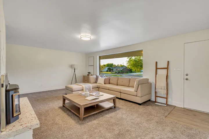 Living area featuring a large picture window, carpet flooring, a built-in fireplace with a light-colored hearth, and a modern flush-mount ceiling light
