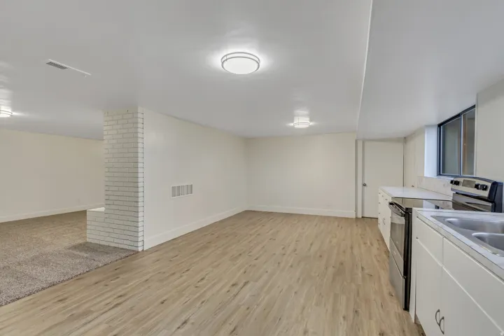 Open living area featuring wood-finish flooring, white cabinetry, a built-in electric range, and a double basin sink