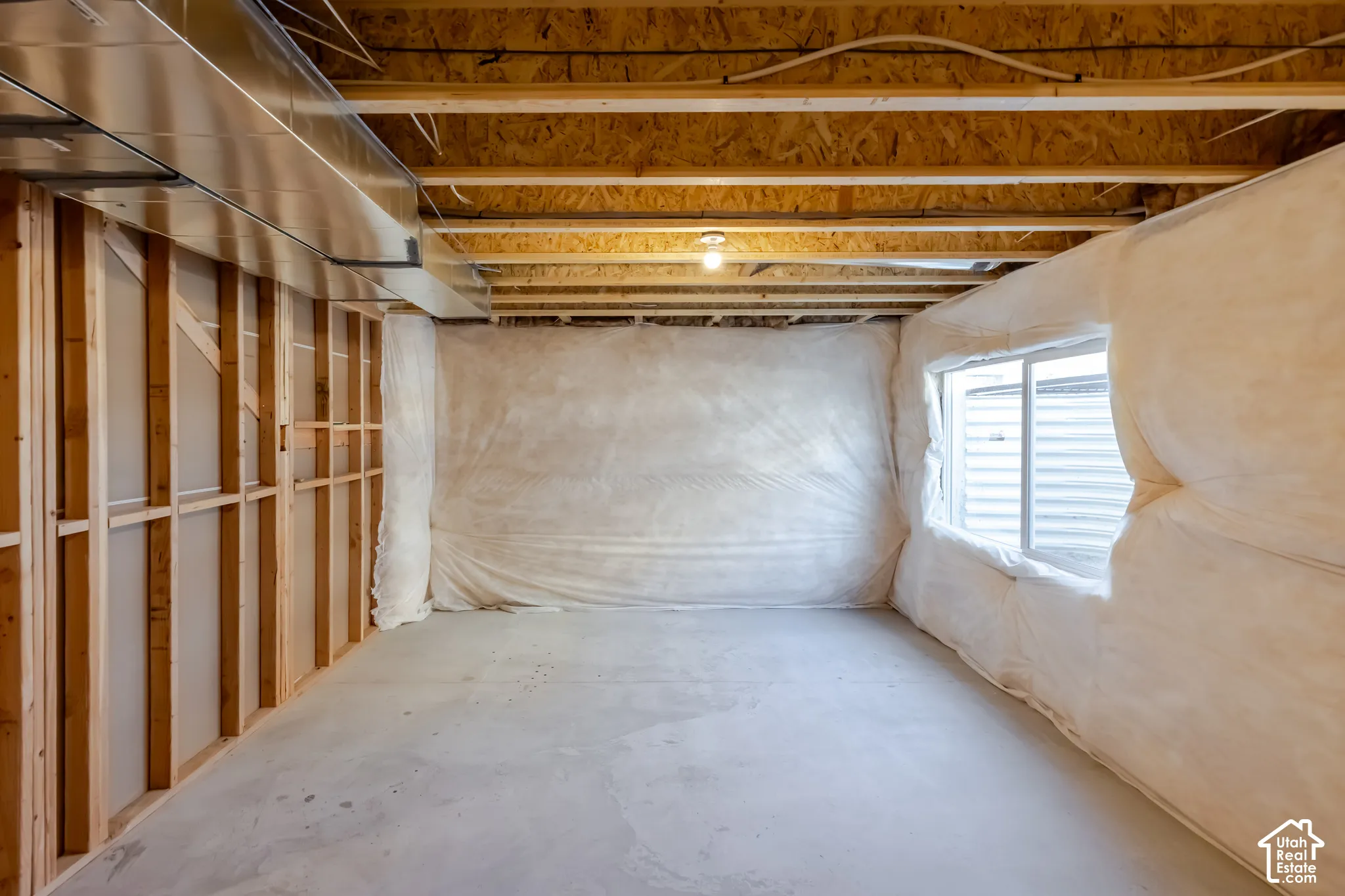 Unfinished space featuring exposed wood-frame wall construction, concrete flooring, insulated wall barriers, a sliding window, and exposed ceiling joists with overhead HVAC ductwork