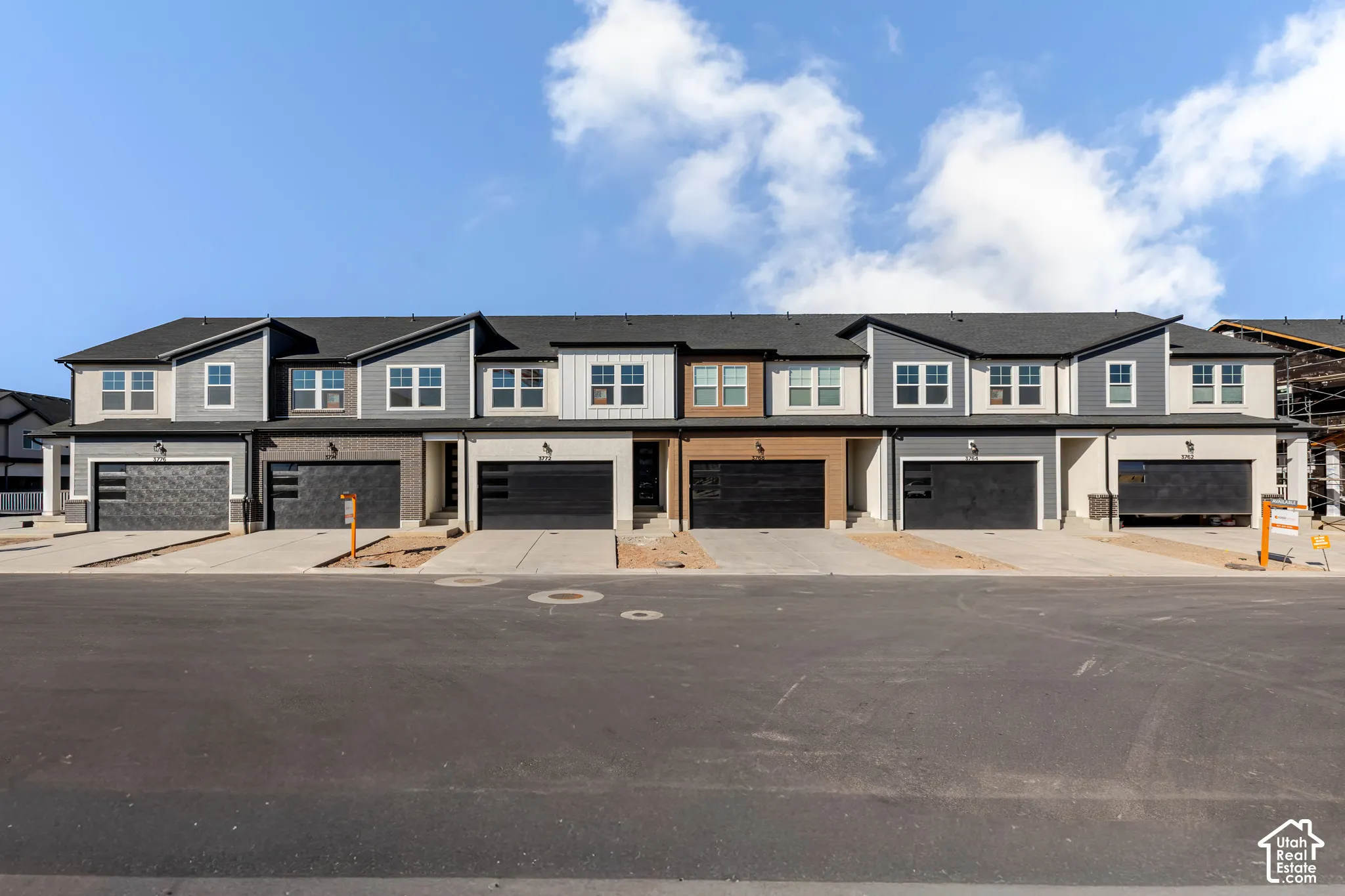 Multi-family exterior featuring varied siding materials, gabled rooflines, dark-toned garage doors with horizontal windows, and concrete driveways