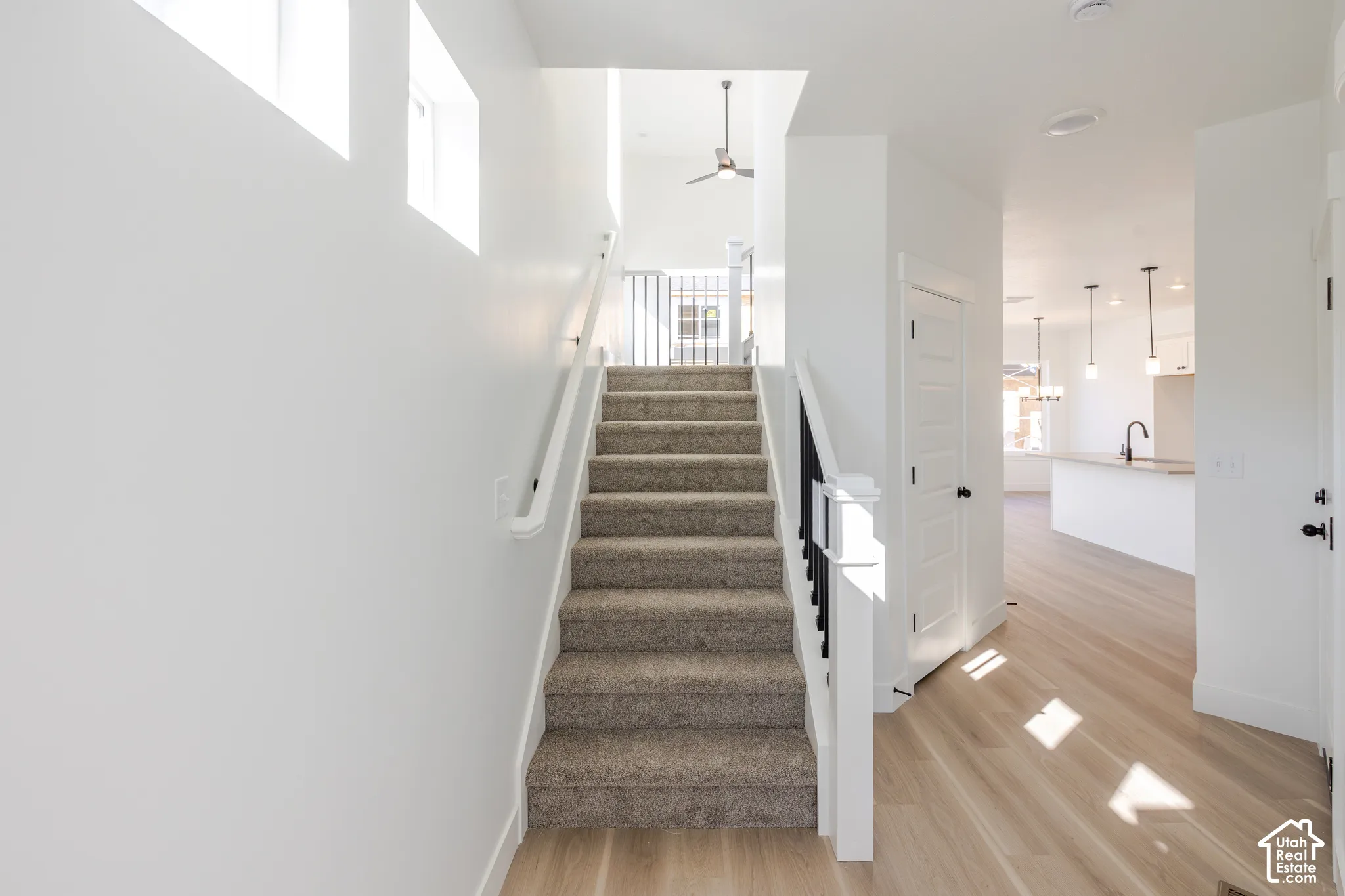 Staircase featuring carpeted steps, a white handrail, and a black-and-white baluster railing, complemented by wood-finish flooring and high-reaching ceilings