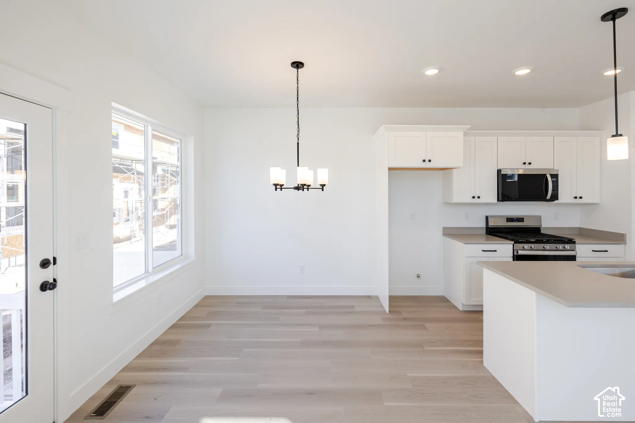 Kitchen featuring white shaker-style cabinetry, a stone-finish countertop, stainless steel appliances, wood-finish flooring, and a multi-light chandelier