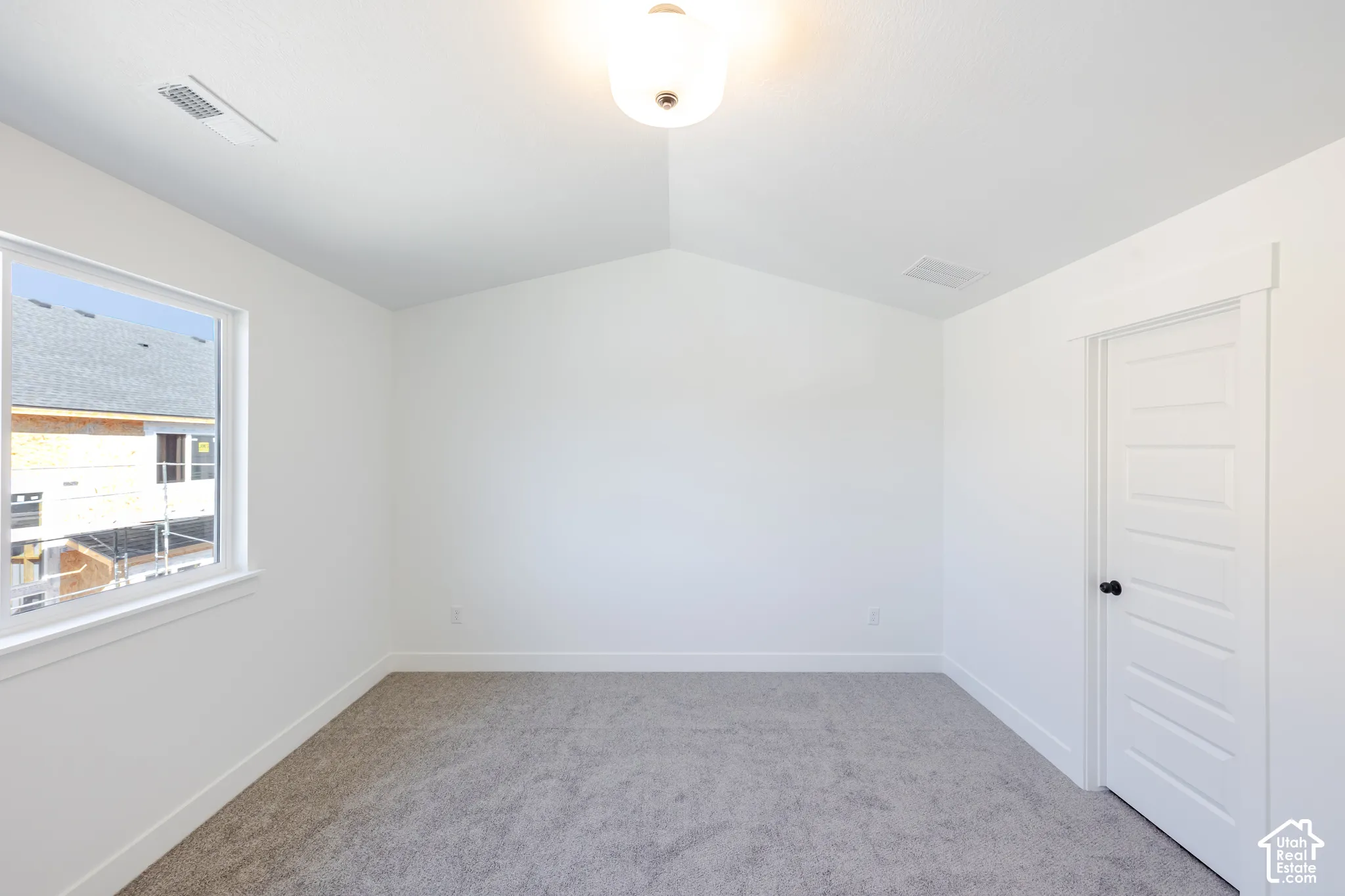 Vaulted ceiling, neutral wall-to-wall carpeting, single-hung window, and a multi-panel interior door with matte black hardware
