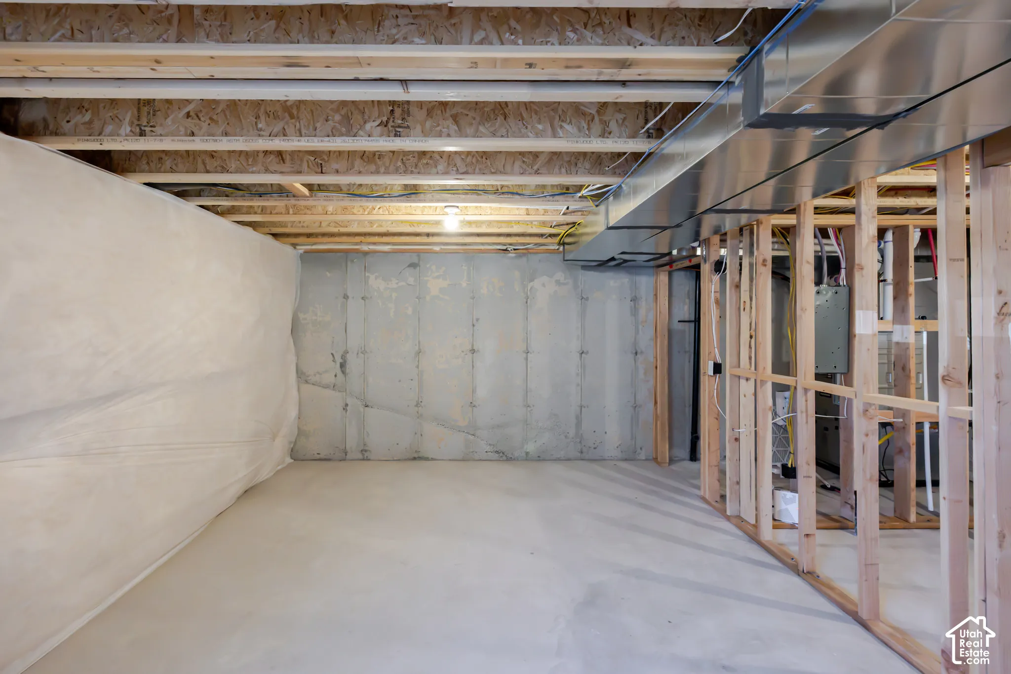 Unfinished lower level featuring exposed wood joist ceiling, concrete floor, reinforced concrete foundation walls, and framed interior wall studs