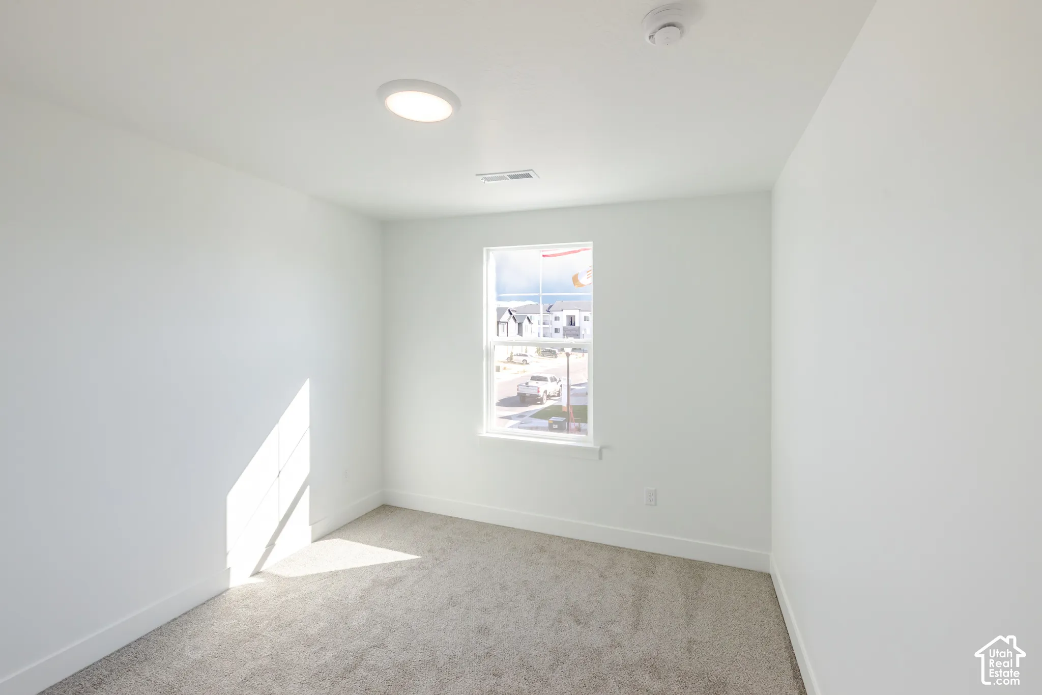 Neutral-toned wall paint, plush carpeting, a single-hung window, and a modern flush-mount LED ceiling light fixture