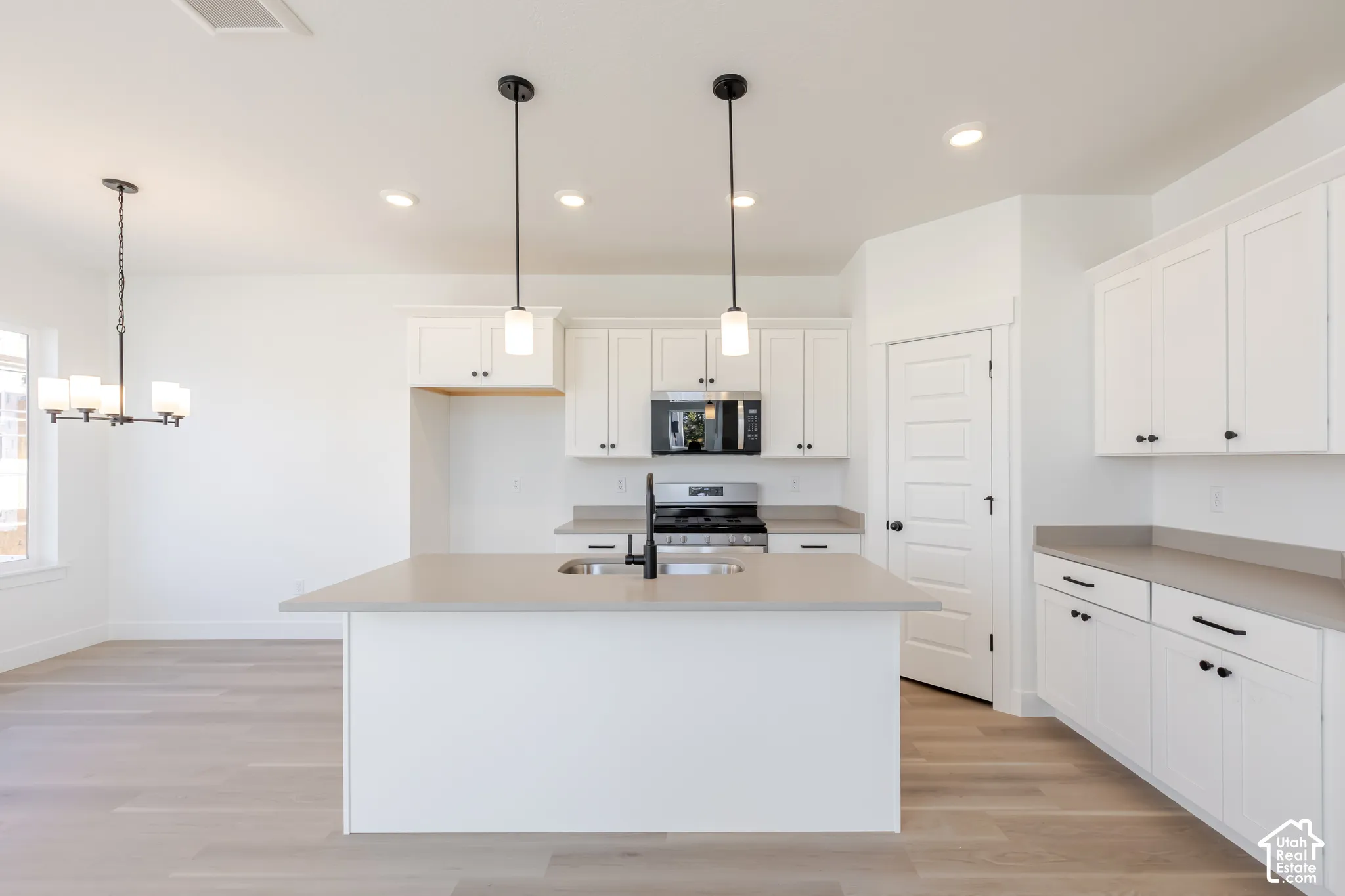 Kitchen featuring white cabinetry, quartz countertops, wood-finish flooring, stainless steel appliances, and dual pendant lighting