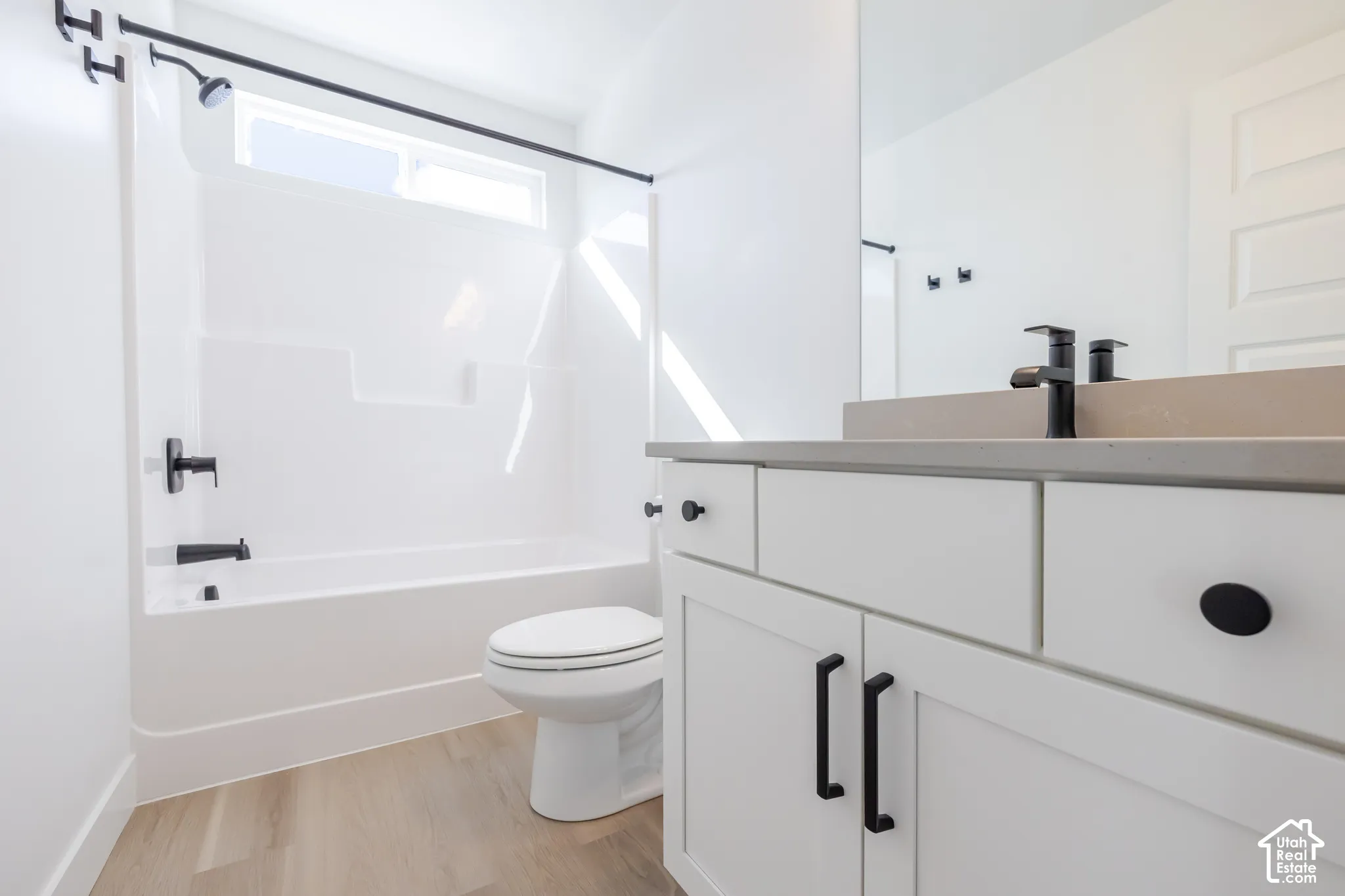 Bathroom featuring white shaker-style vanity cabinetry, a solid surface countertop, matte black hardware, and a tub-shower combination with matte black fixtures and wood-finish flooring