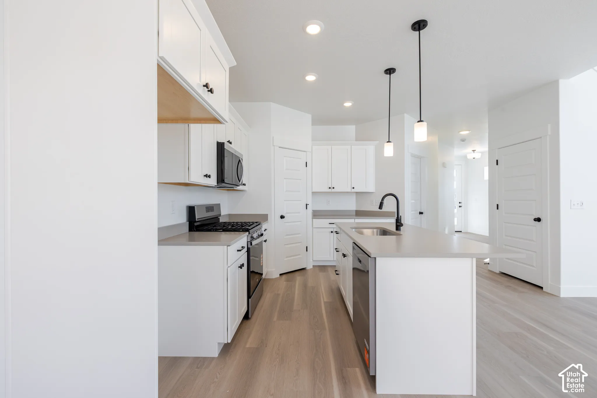 Kitchen featuring white shaker-style cabinetry, solid-surface countertops, a center island with an undermount sink and matte black faucet, and wood-finish flooring