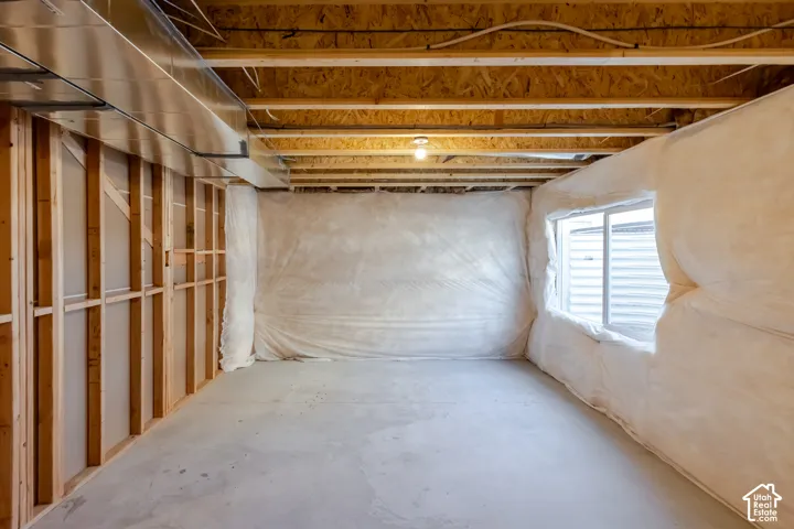 Unfinished space featuring exposed wood-frame wall construction, concrete flooring, insulated wall barriers, a sliding window, and exposed ceiling joists with overhead HVAC ductwork