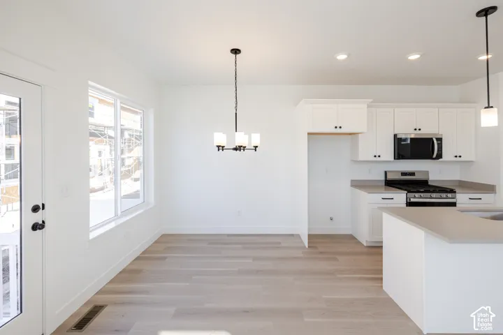 Kitchen featuring white shaker-style cabinetry, a stone-finish countertop, stainless steel appliances, wood-finish flooring, and a multi-light chandelier