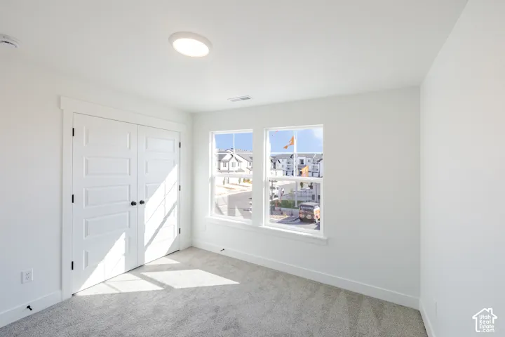 Neutral-toned carpeted flooring, dual-panel closet doors, and dual windows with white trim