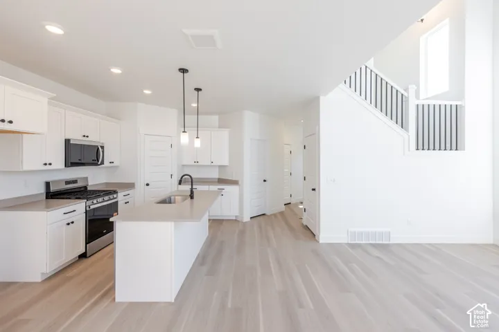 Kitchen featuring white cabinetry, solid-surface countertops, wood-finish flooring, a central island with a matte black faucet, and a staircase with a black-and-white balustrade