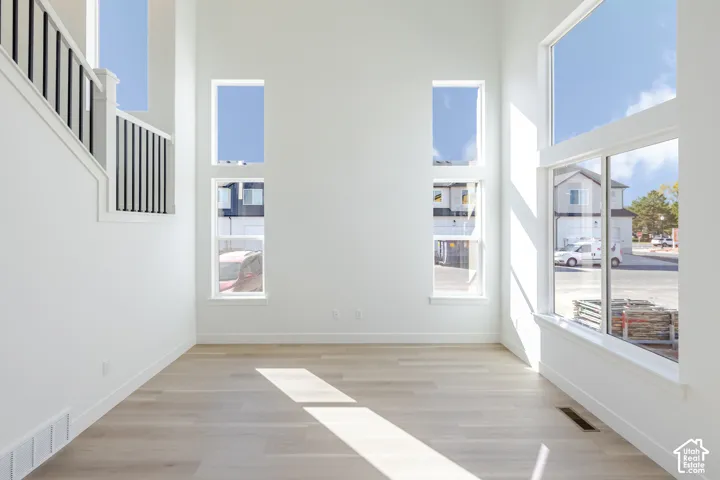 Double-height ceiling, floor-to-ceiling windows, light-toned wood-finish flooring, and a staircase featuring a white railing with black balusters