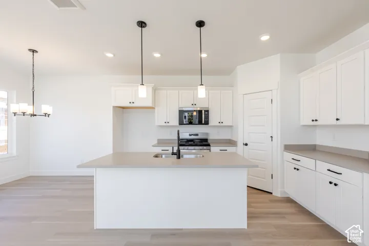 Kitchen featuring white cabinetry, quartz countertops, wood-finish flooring, stainless steel appliances, and dual pendant lighting