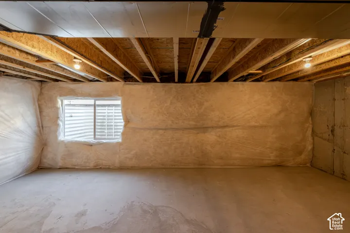 Unfinished interior space featuring exposed wood joist ceilings, insulated wall vapor barriers, a concrete floor, and a sliding egress window