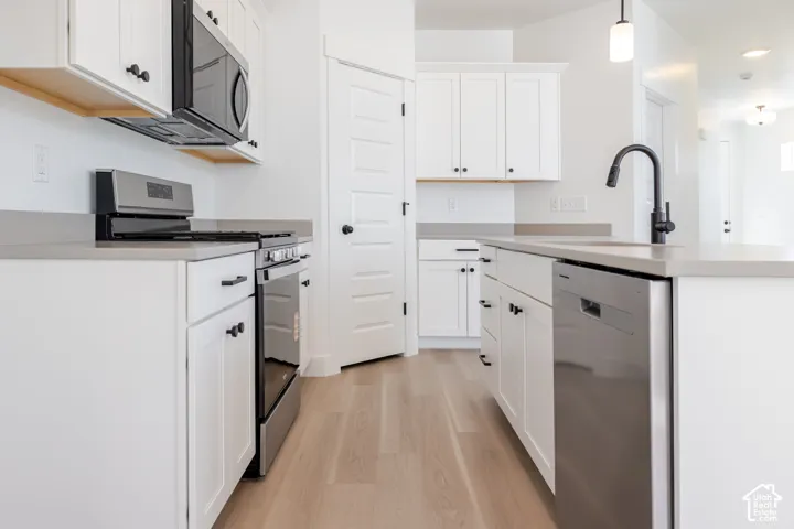 Kitchen featuring white shaker-style cabinetry, solid-surface countertops, wood-finish flooring, stainless steel appliances, and a matte black pull-down faucet