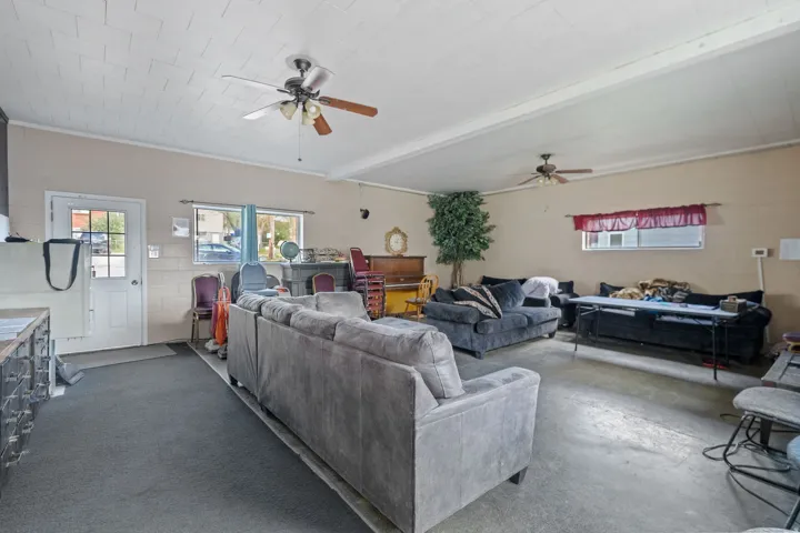 Spacious interior area featuring a combination of concrete and carpeted flooring, two ceiling fans, white trim, and multiple windows