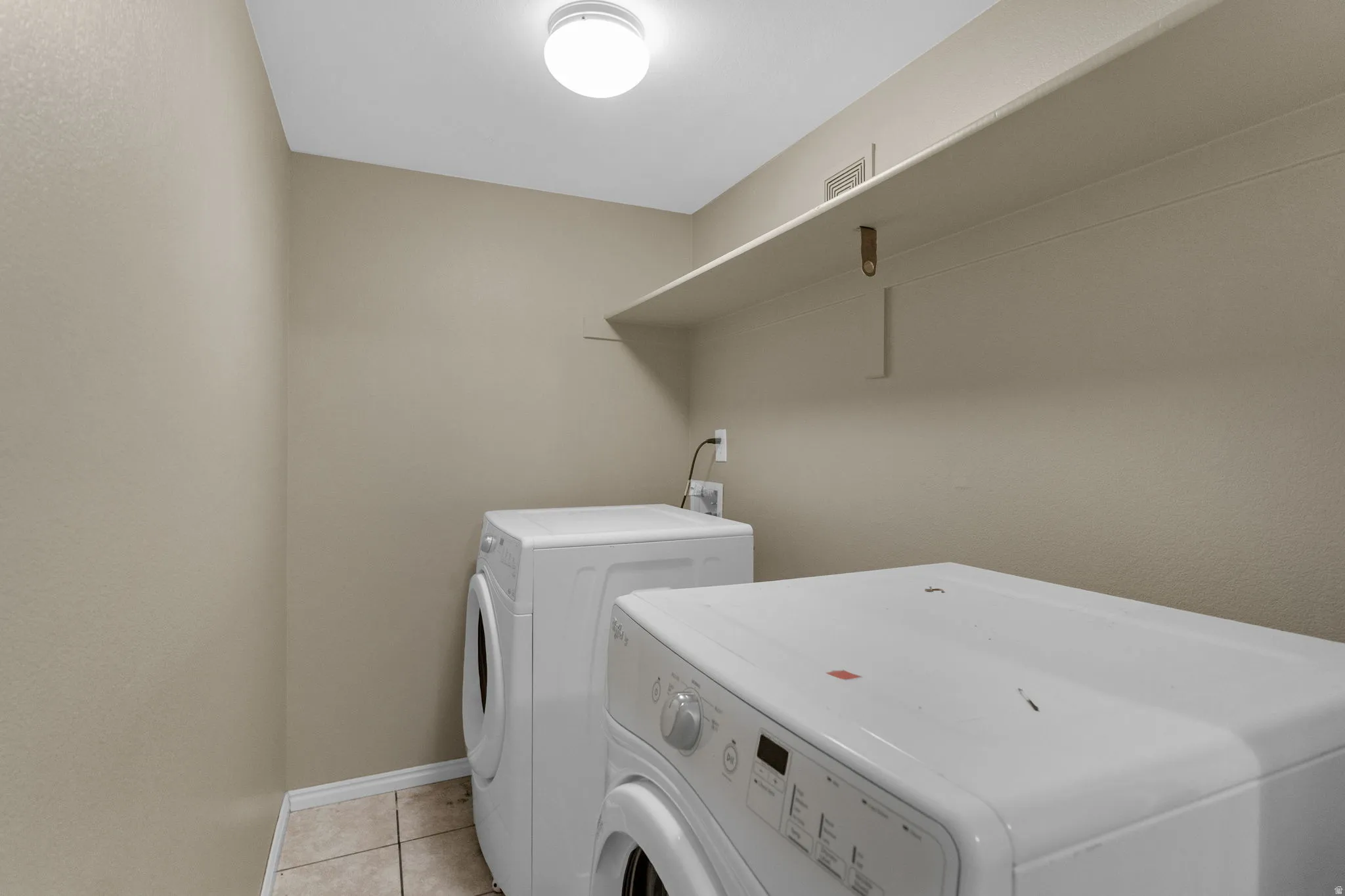 Dedicated utility area featuring a built-in overhead shelf for storage, neutral wall tones, and ceramic tile flooring