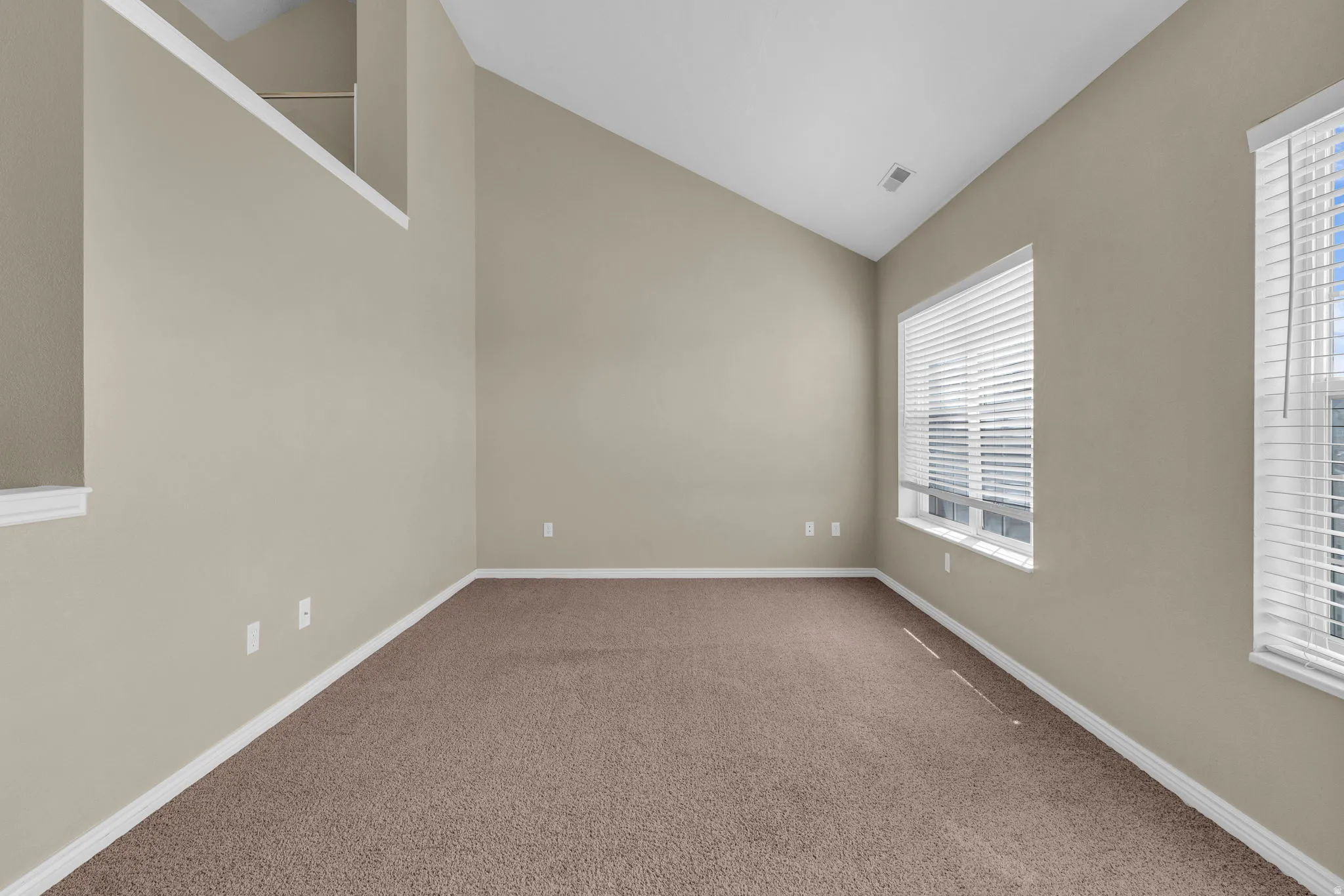 Lofted room featuring vaulted ceilings, light-colored walls, brown carpet flooring, and two large windows with blinds