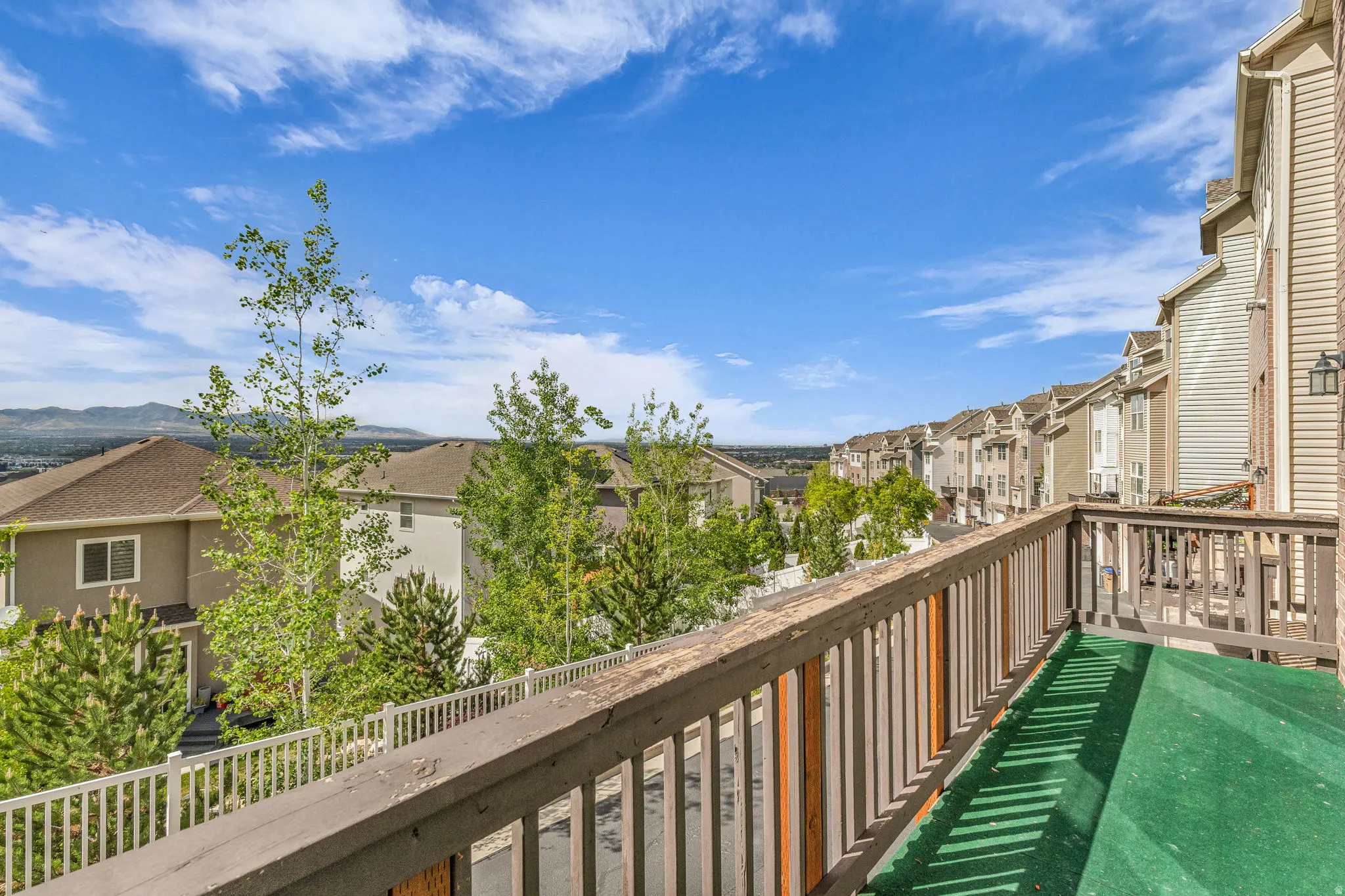 Outdoor balcony featuring a wooden railing, green artificial turf flooring, and a residential community backdrop